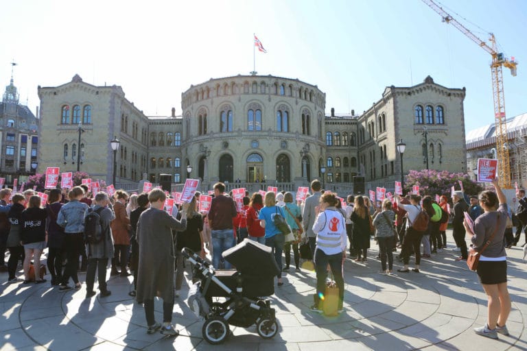 En protest foran Stortinget. Mange av de som er på markeringen holder opp plakater med slagord og Redd Barna-logoen.