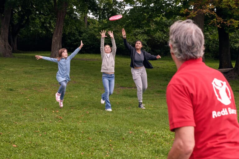 Tre barn prøver å fange en frisbee kastet av en Redd Barna-frivillig