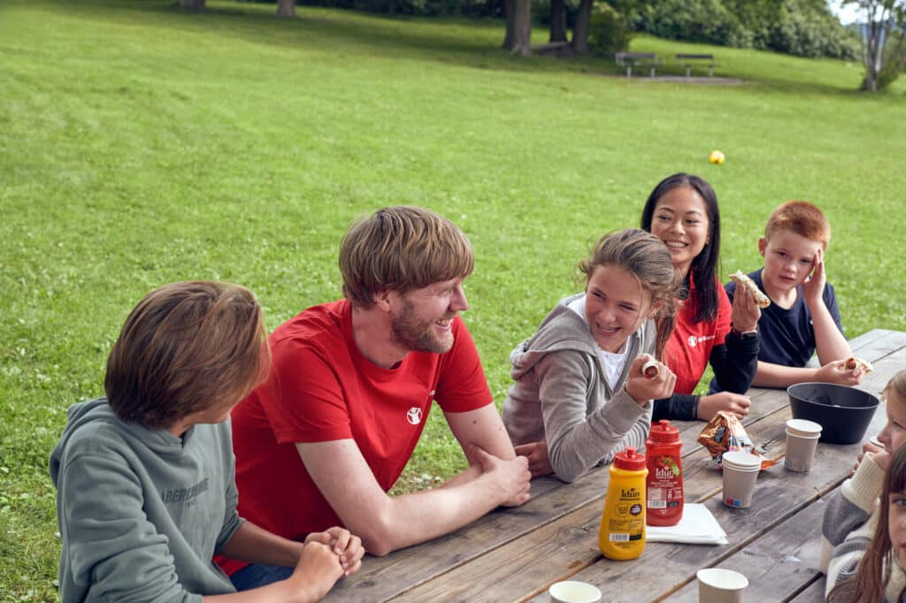 Barn og Redd Barna-frivillige smiler og ler av noe i en park