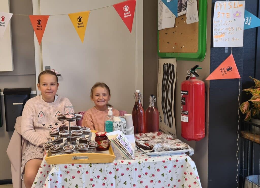 to barn som smiler, de holder basar og selger kake og saft