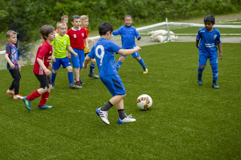 En gjeng med unge gutter spiller fotball i fotballdraker på en gressbane.