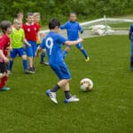 En gjeng med unge gutter spiller fotball i fotballdraker på en gressbane.