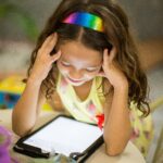 En liten jente med regnbuehårbøyle som ser på et nettbrett