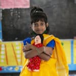 Amina, 6, holding a doll in her classroom